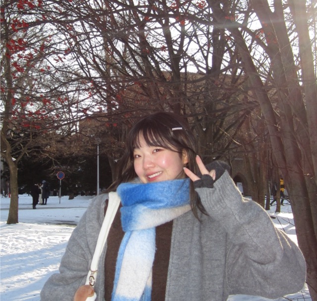 Nichole Tian smiling and holding up her hand in a peace sign in a snowy area with trees in the background.